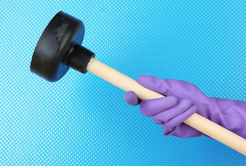 Gloved hand holding a plunger against blue background