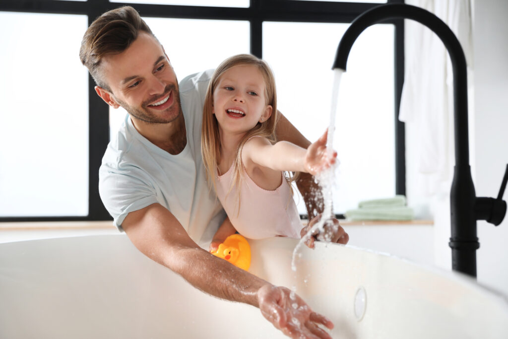 Father and daughter fill bath tub with hot water