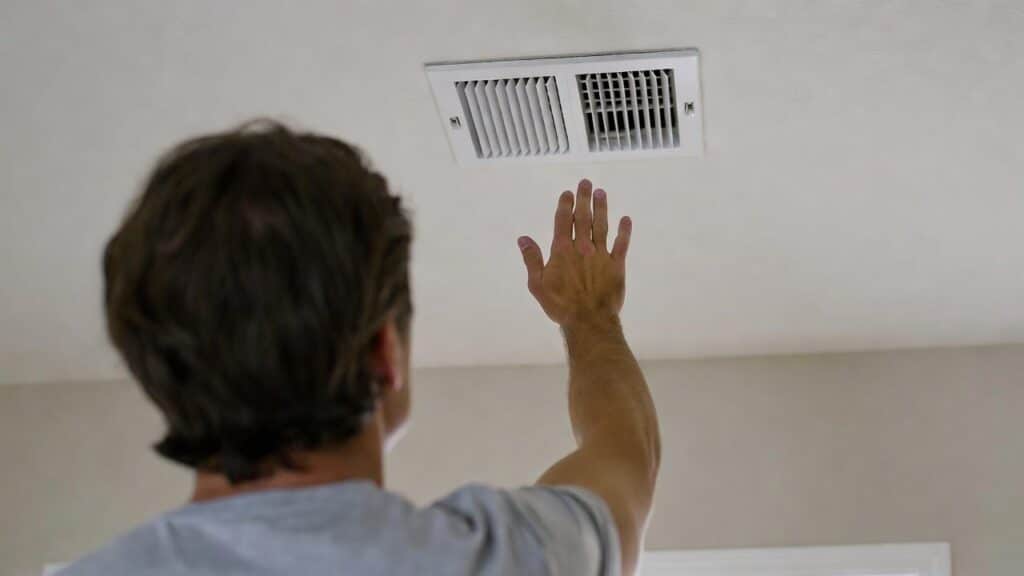 a homeowner holds his hand to the air supply wondering why is my air conditioner not cooling