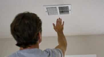 a homeowner holds his hand to the air supply wondering why is my air conditioner not cooling