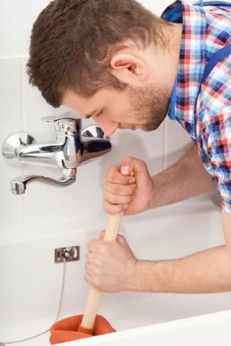 Man using a plunger to unclog a bathtub drain