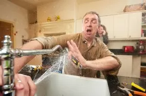 Man reacting to burst kitchen faucet spraying water during plumbing emergency